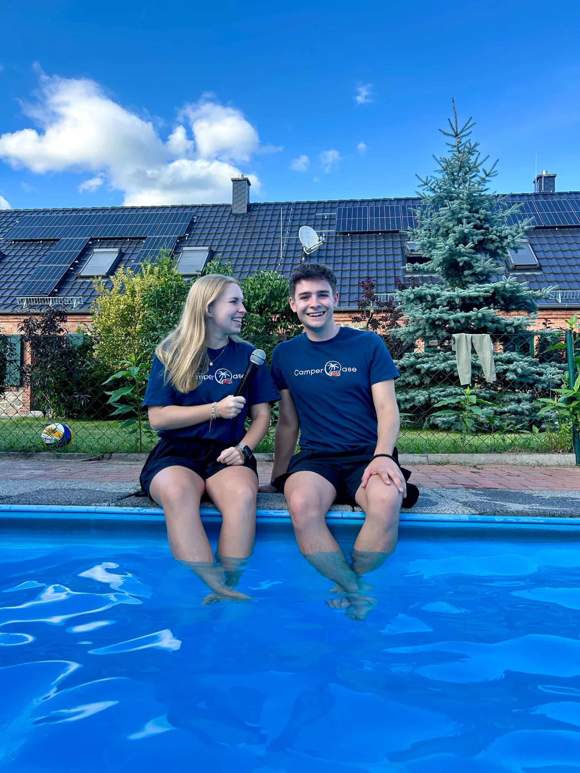Zwei junge Kollegen sitzend am Poolrand mit einem Podcastmikrofon in der Hand