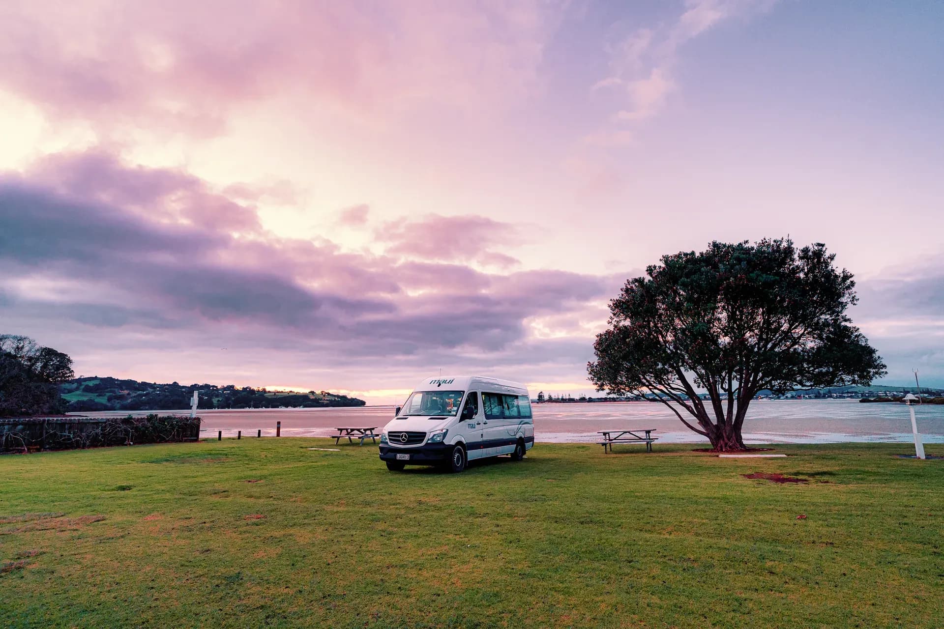 Ultima von Maui Motorhomes neben Baum vor See in Neuseeland bei rötlichem Licht