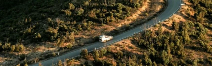 Camper fährt auf Straße zwischen Wäldern Vogelperspektive