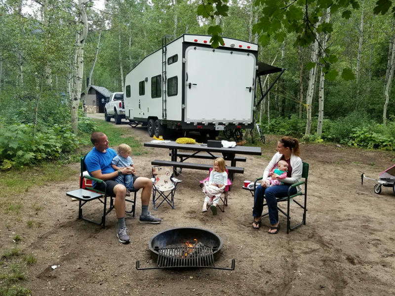 Familie sitzt auf Campingstühlen vor Grill