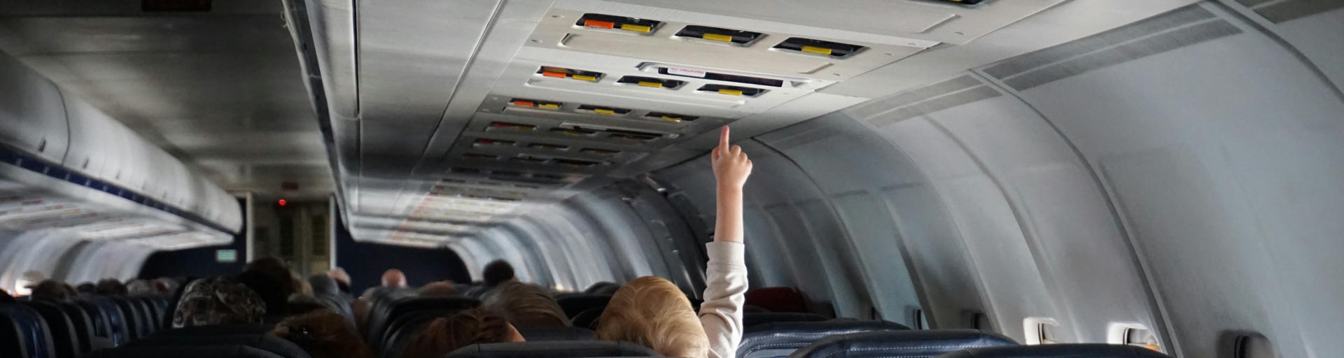 Kind sitzt im Flugzeug und hebt den Zeigfinger ume inen Knopf zu drücken
