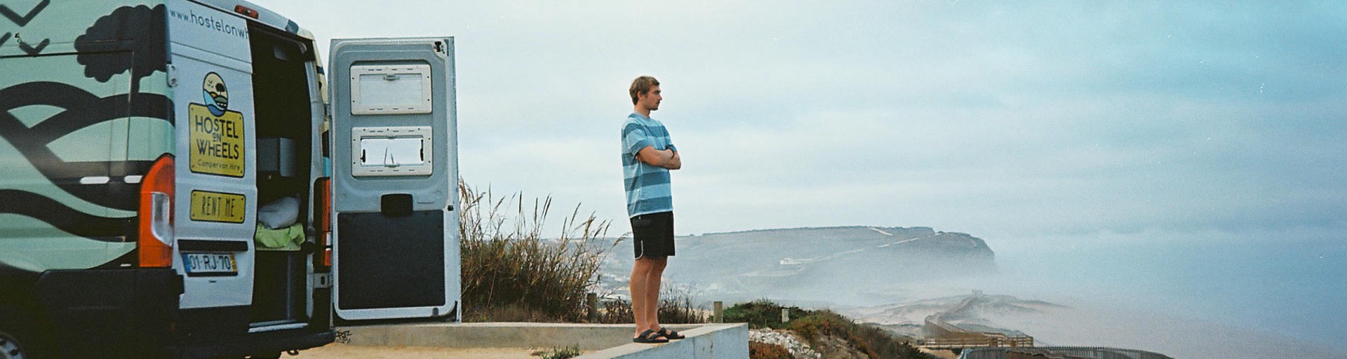 Mann steht vor Camper in Portugal und blickt aufs Meer