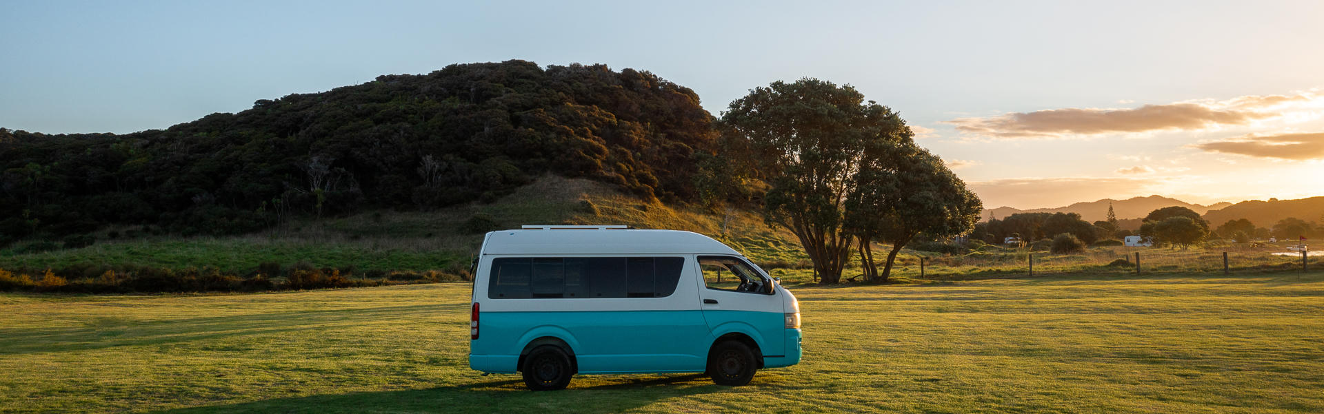 Der Willy Camper von Barefoot Camper in Neuseeland auf einer grünen Wiese.