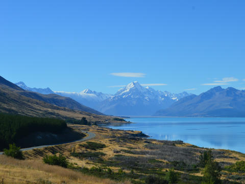 Eine gewundene Straße führt am Lake Pukaki in Neuseeland entlang in verschneite Berge