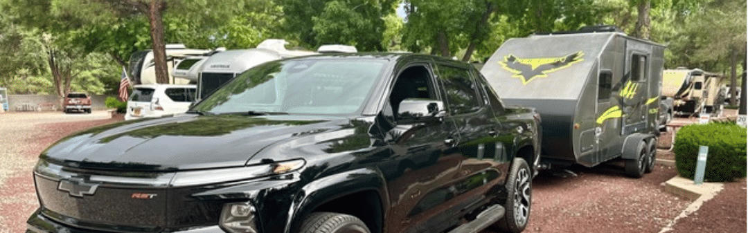 Der PickUp Truck mit Wohnwagen elektrisch geparkt auf einem Campingplatz. 